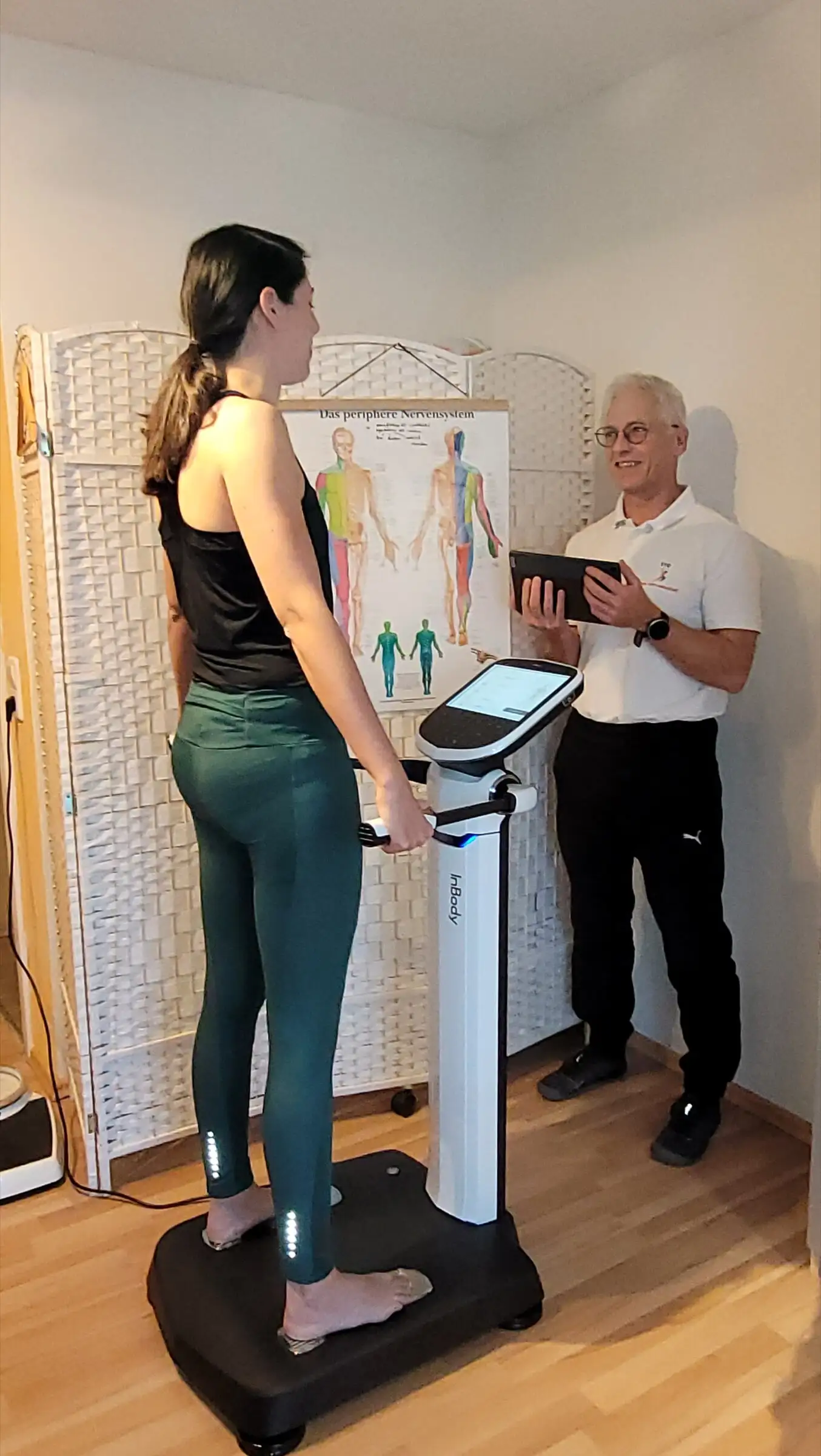 Kundin steht auf der InBody-Waage, Uwe Schapeit wertet die Körperanalyse am Tablet aus