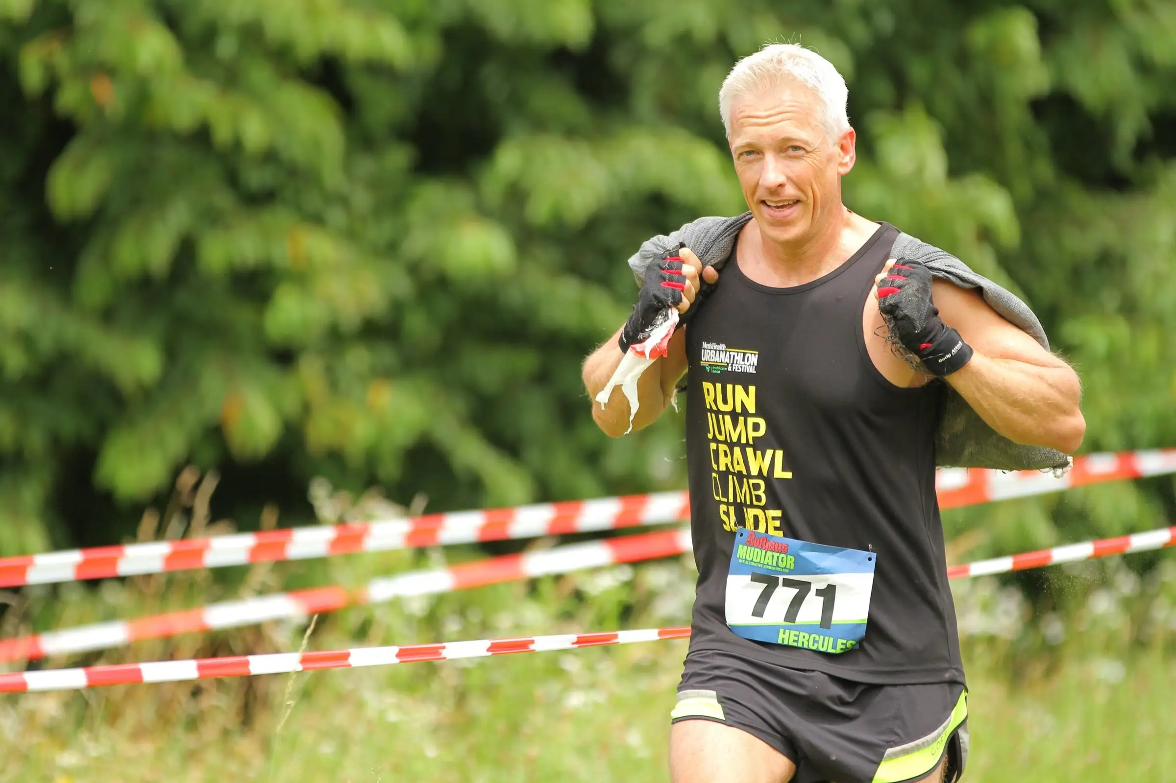 Uwe Schapeit beim Hindernislauf mit Startnummer 771, einen Sandsack über der Schulter