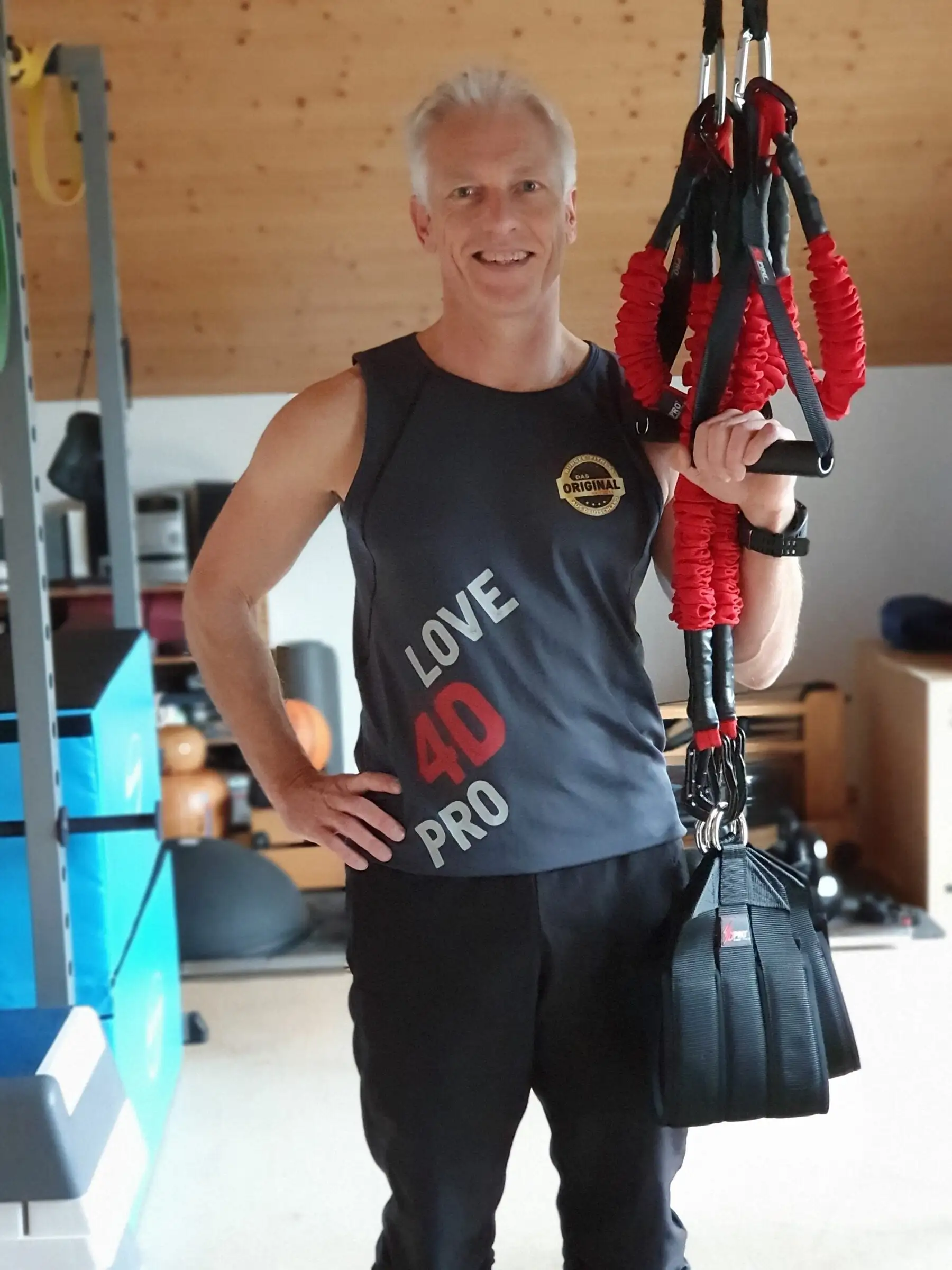 Uwe Schapeit steht lachend neben dem 4D PRO Schlingentrainer und hält die roten Bungee-Seile in der Hand