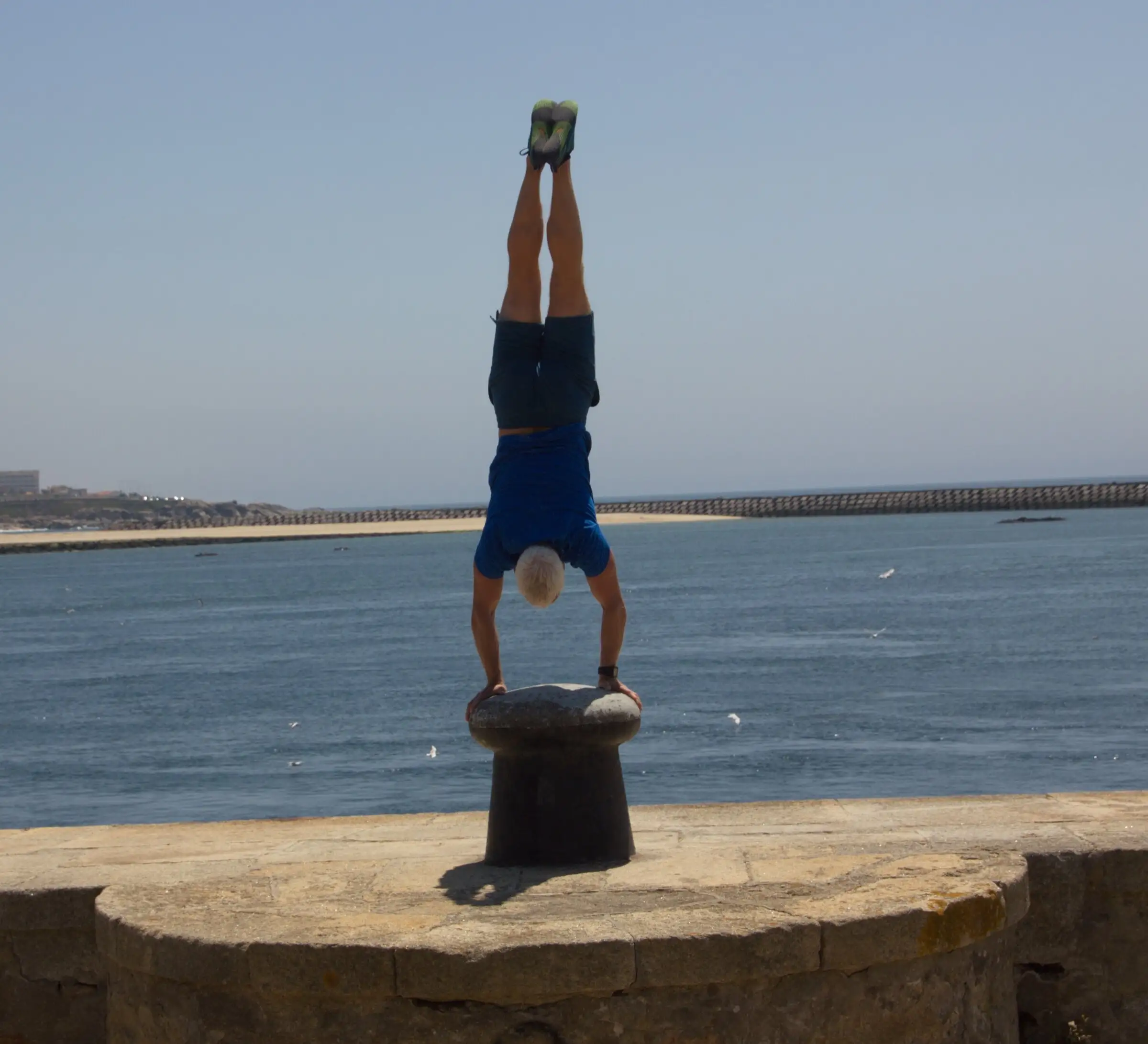 Uwe Schapeit macht einen Handstand auf einem Poller an der Mole, dahinter das Meer