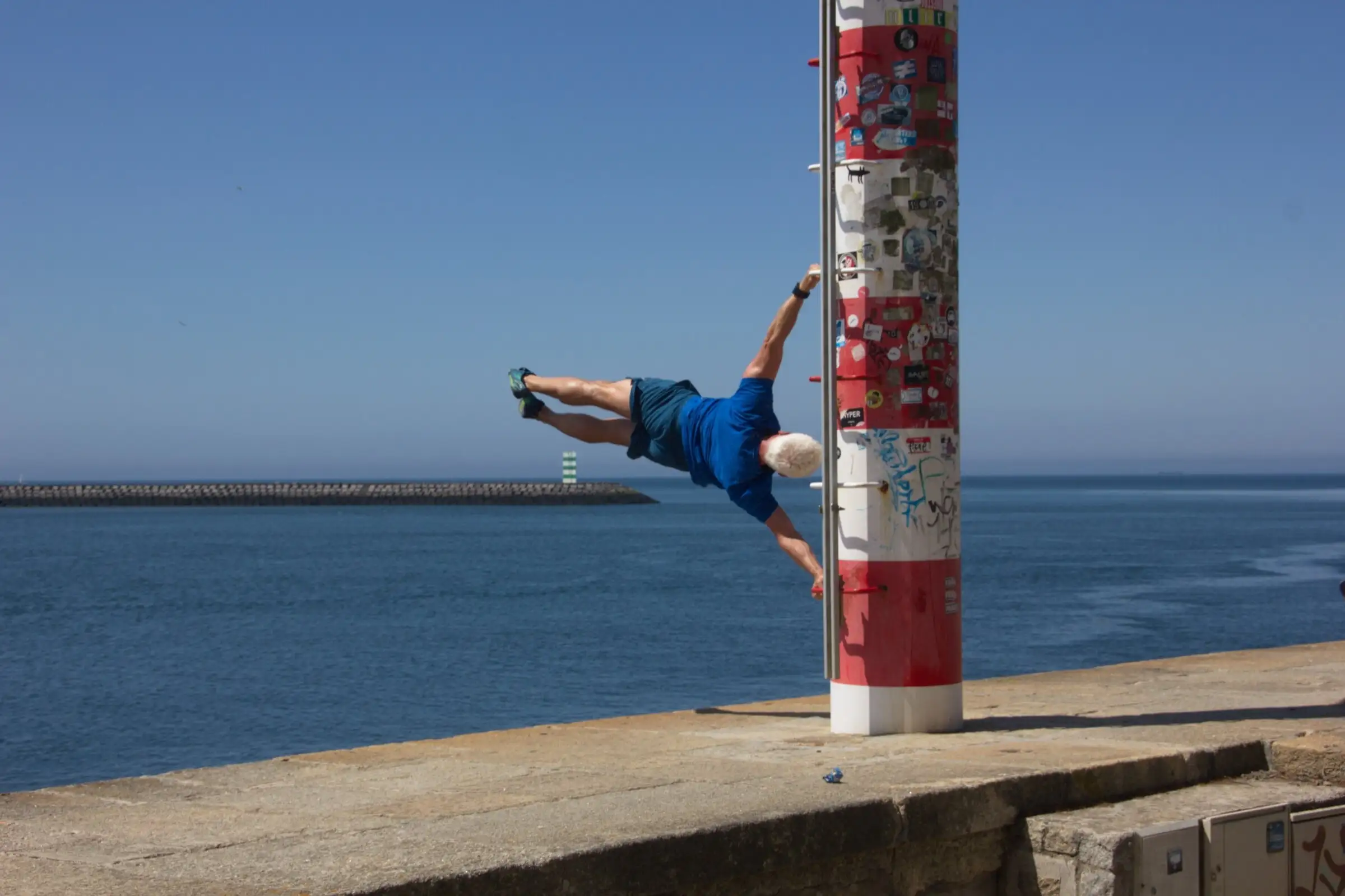 Uwe Schapeit hält sich waagerecht an einem Pfahl an der Mole, die Übung Human Flag
