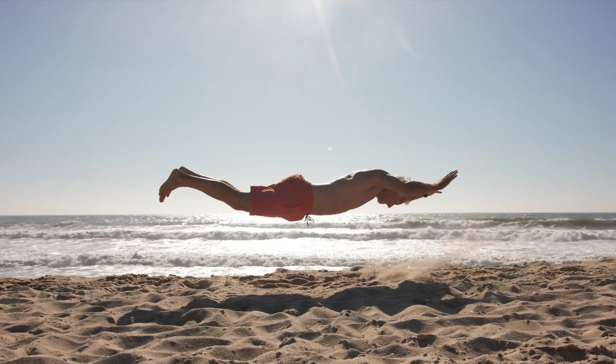 Silhouette von Uwe Schapeit im Sprung waagerecht über dem Strand im Gegenlicht