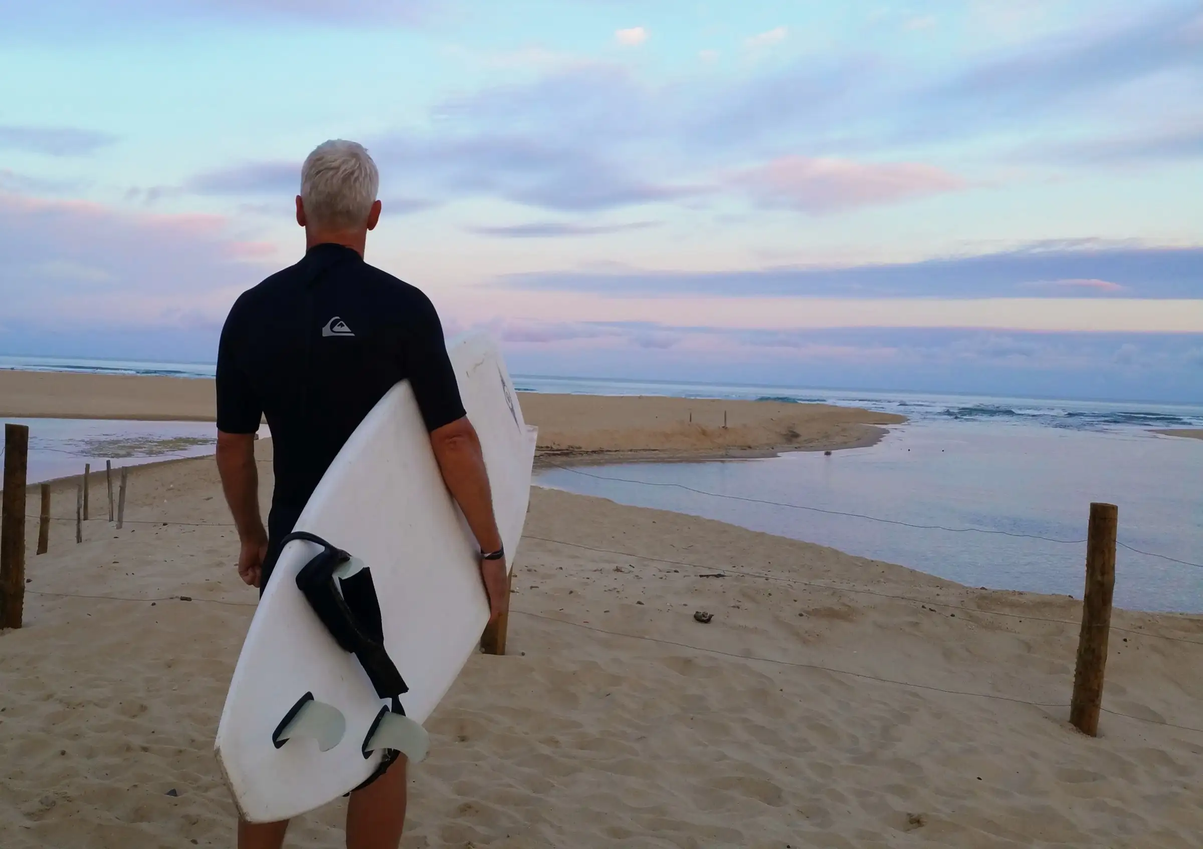 Uwe Schapeit steht mit dem Surfbrett unter dem Arm am Strand und schaut aufs Meer